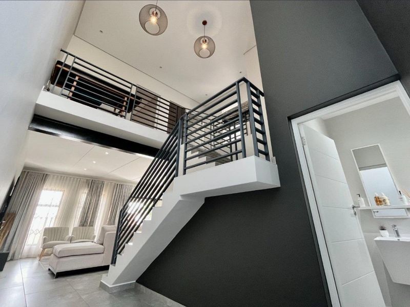 Modern double-volume entrance hall featuring a sleek staircase with metal balustrades, mezzanine level, and access to a guest bathroom with contemporary finishes.