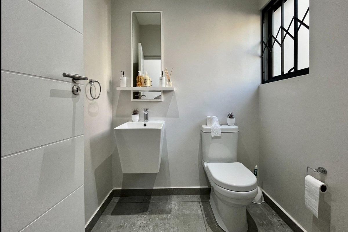 A modern, well-maintained guest bathroom featuring a wall-mounted basin, toilet, and neutral tiled flooring with a secure window.