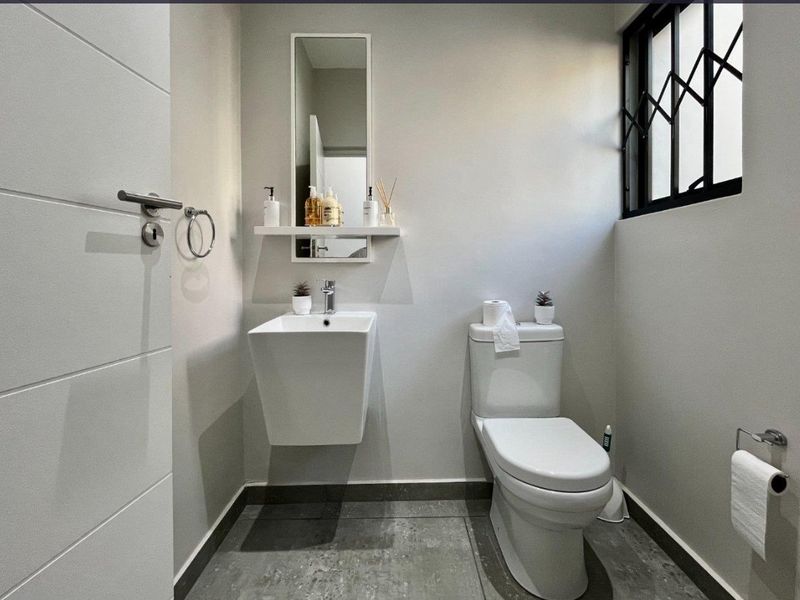 A modern, well-maintained guest bathroom featuring a wall-mounted basin, toilet, and neutral tiled flooring with a secure window.
