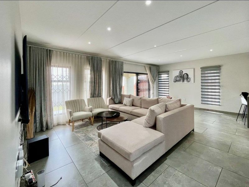 Spacious living room featuring large format floor tiles, recessed ceiling lighting, and expansive windows with integrated blinds and curtain tracks for natural light.