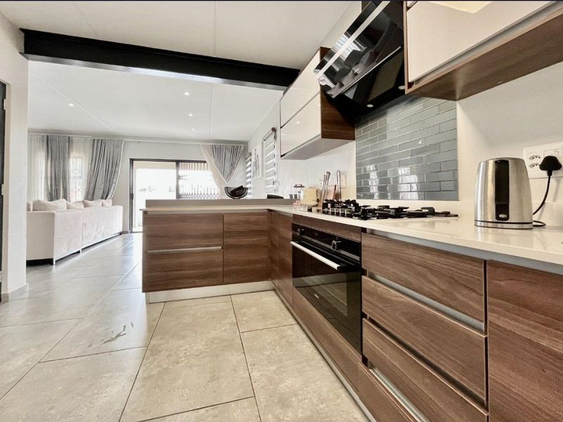 Modern open-plan kitchen featuring sleek wood-finish cabinetry, stone countertops, subway tile backsplash, and high-quality built-in appliances, seamlessly flowing into the living area.