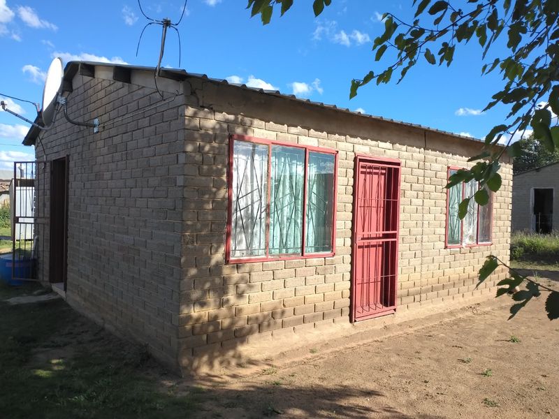 A single-story house featuring exposed brick construction, metal security gates, and metal-framed windows under a corrugated metal roof.