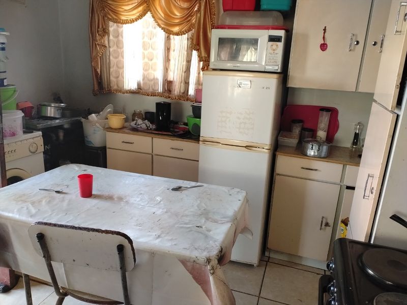 A dated kitchen featuring original cabinetry, laminate countertops, and tiled flooring, offering significant potential for modernization and renovation.