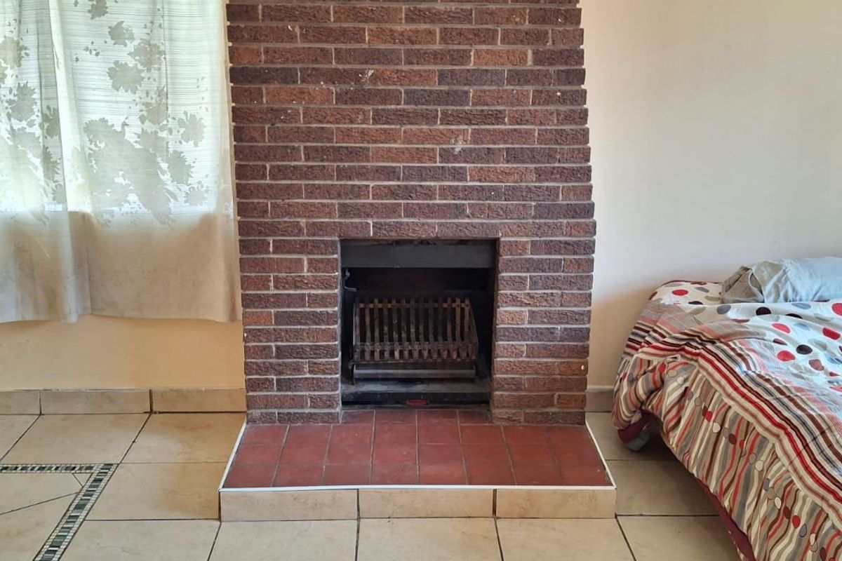 A living room featuring a prominent brick fireplace with a tiled hearth and ceramic floor tiles throughout.