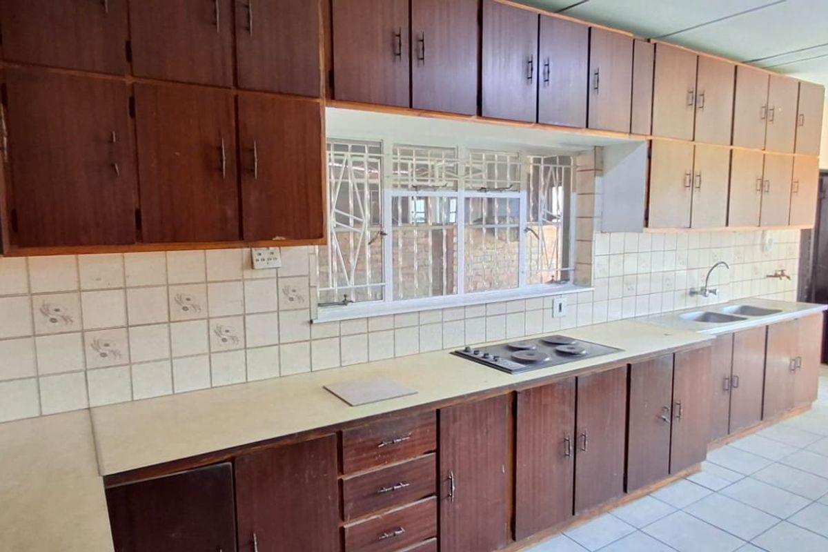 A spacious, dated kitchen featuring extensive wooden cabinetry, laminate countertops, a built-in hob, and a double sink, offering significant potential for modernization.