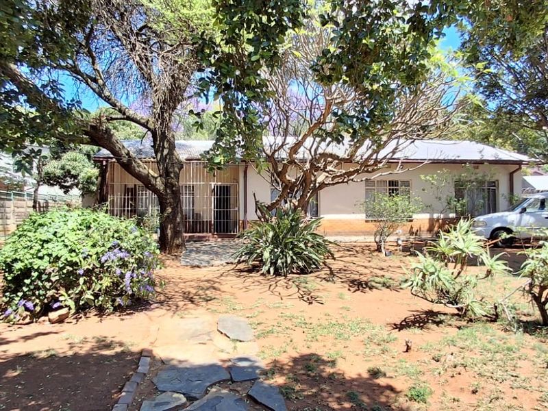 Front view of a single-story house featuring a large garden with mature trees, stone pathway, and security gates on the windows.