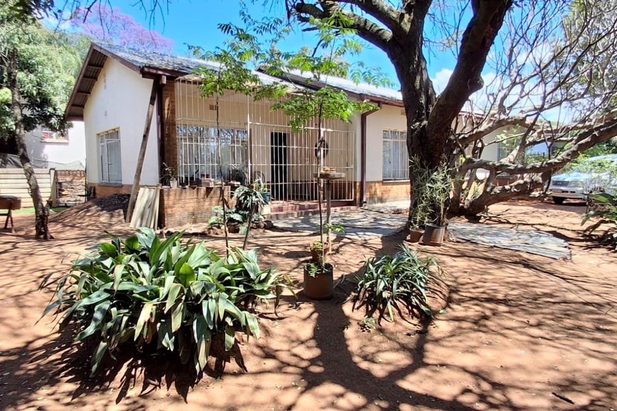 Rear view of a single-story house featuring a tiled roof, brick accents, and security gates, set within a large, mature garden area.