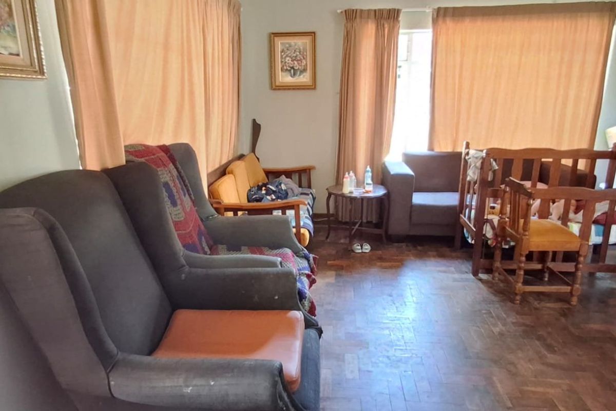 A living room featuring traditional parquet flooring and large windows with curtain rails, offering a functional space with potential for modernization.