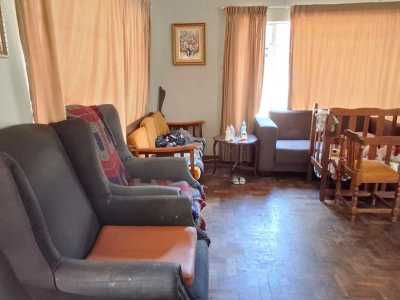 A living room featuring traditional parquet flooring and large windows with curtain rails, offering a functional space with potential for modernization.