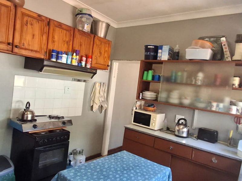 A functional kitchen featuring wooden cabinetry, a tiled splashback, and built-in shelving, offering a dated aesthetic with potential for modernization.