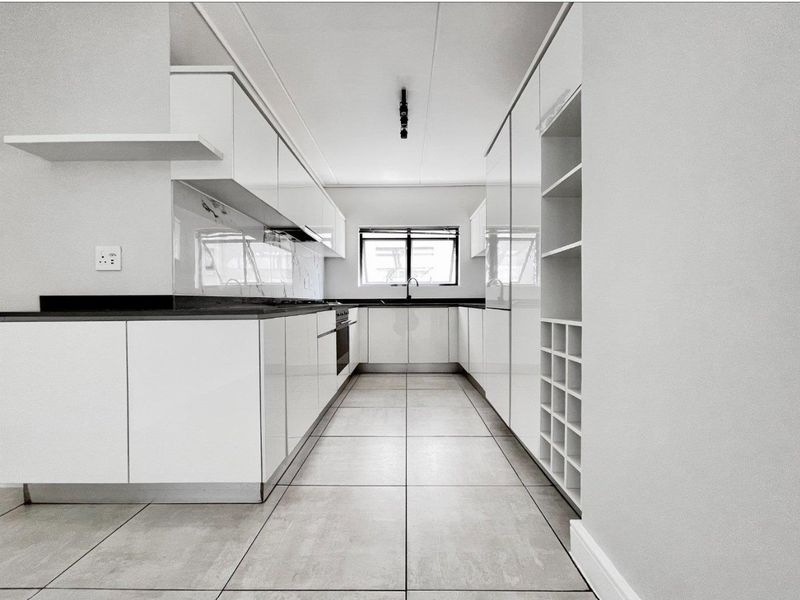 Modern galley-style kitchen featuring sleek white cabinetry, dark stone countertops, integrated appliances, and large format floor tiles.