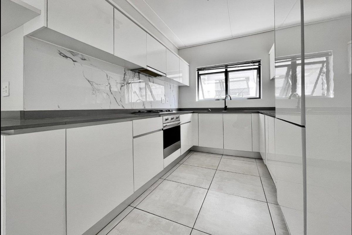 Modern kitchen featuring sleek white glossy cabinetry, marble-look splashback, stone countertops, built-in oven, gas hob, and high-quality tiled flooring.