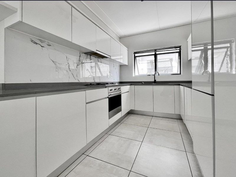 Modern kitchen featuring sleek white glossy cabinetry, marble-look splashback, stone countertops, built-in oven, gas hob, and high-quality tiled flooring.