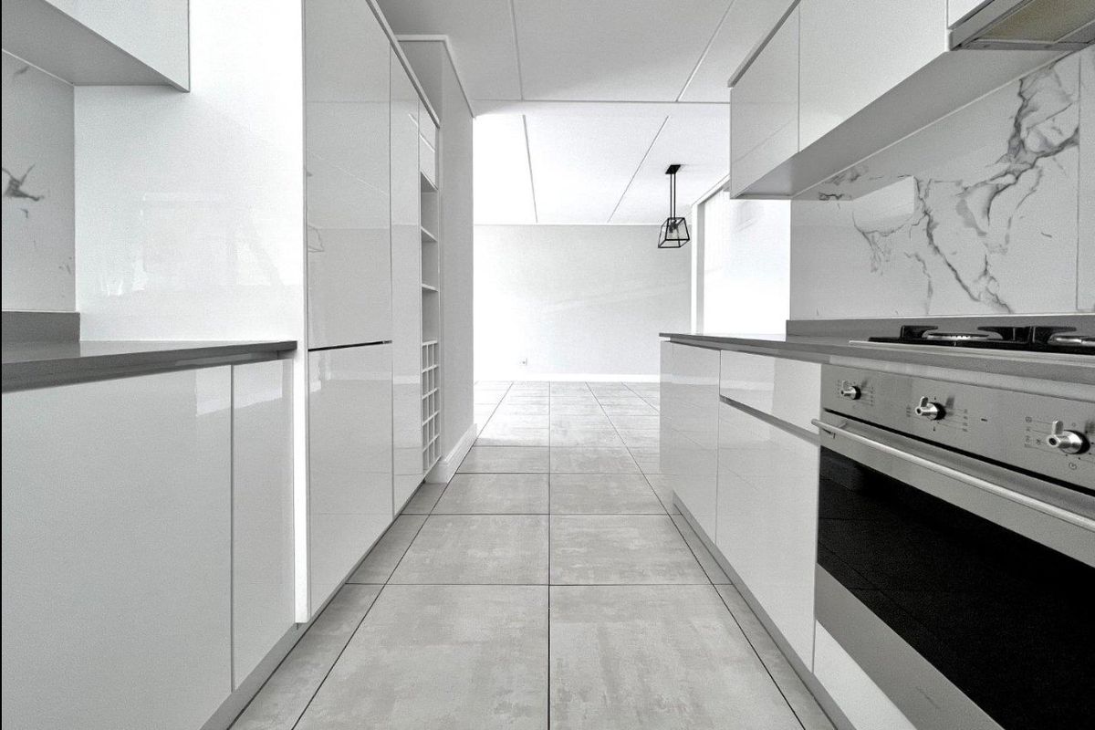 Modern galley-style kitchen featuring high-gloss white cabinetry, integrated oven, gas cooktop, and marble-look splashback with neutral tiled flooring.