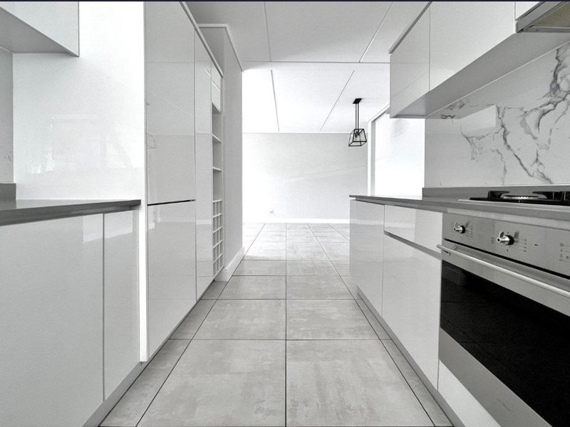 Modern galley-style kitchen featuring high-gloss white cabinetry, integrated oven, gas cooktop, and marble-look splashback with neutral tiled flooring.