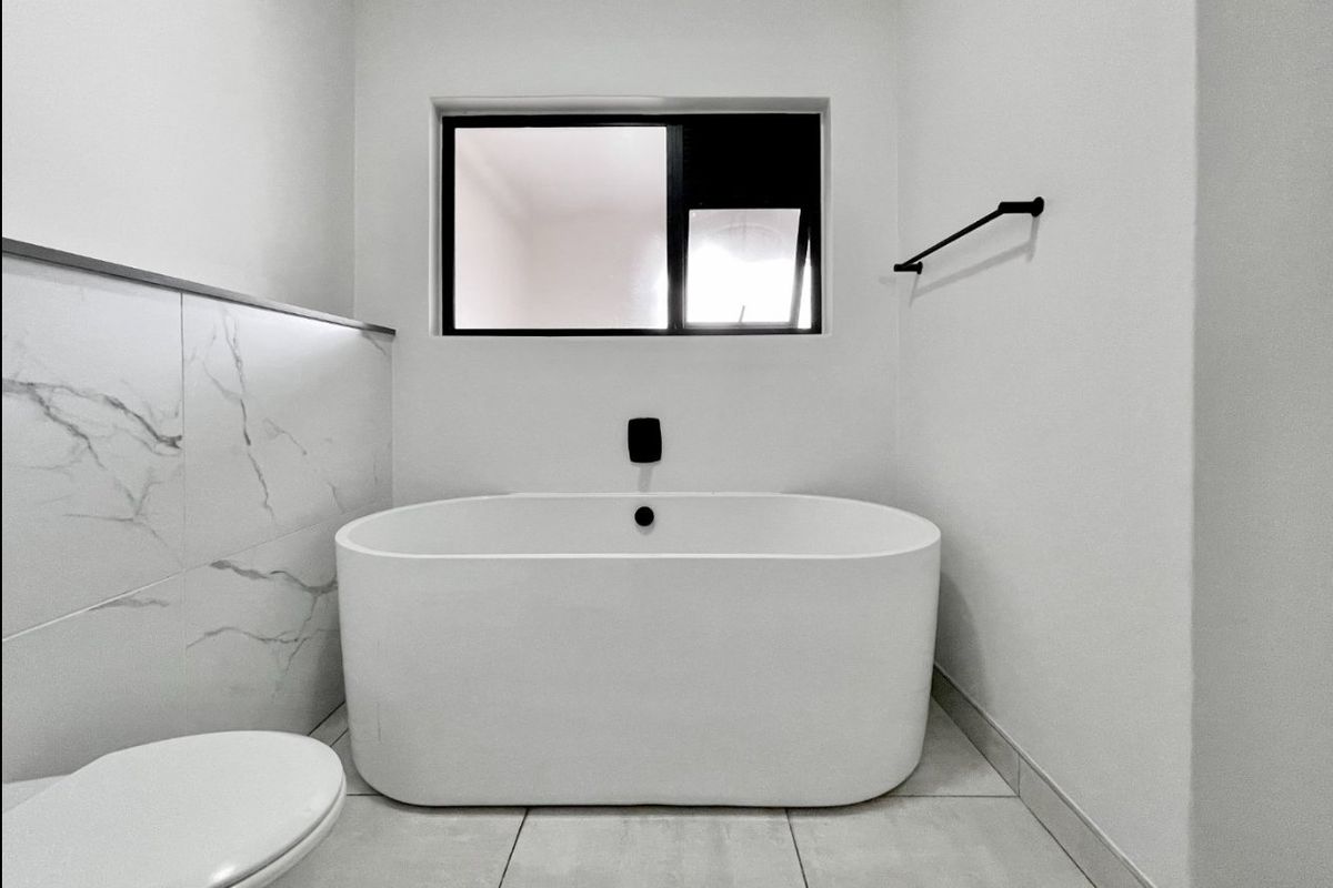 Modern bathroom featuring a sleek freestanding bathtub, contemporary black fixtures, and elegant marble-look wall tiling.