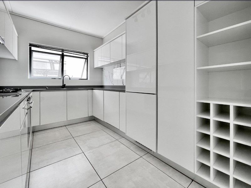 Modern, well-appointed kitchen featuring sleek white cabinetry, stone countertops, integrated appliances, and a dedicated wine rack, finished with contemporary tiled flooring.