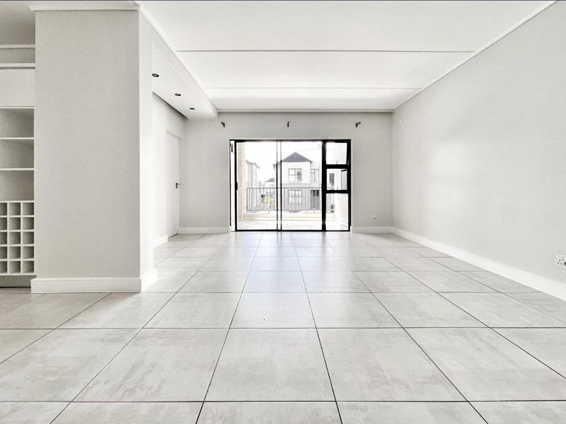 A bright and spacious open-plan living area featuring neutral tiled flooring, recessed lighting, and a large sliding glass door leading to an outdoor space.