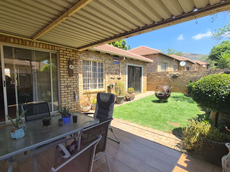 A covered patio area featuring tiled flooring and a brick facade, overlooking a private garden with a lawn and brick boundary wall.