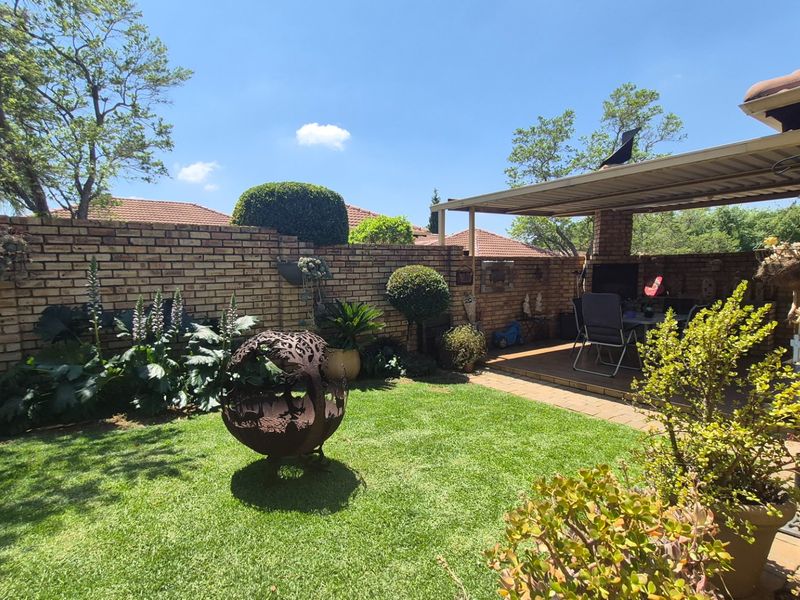 A private rear garden featuring a well-maintained lawn, brick boundary walls, and a covered patio area with a built-in braai.