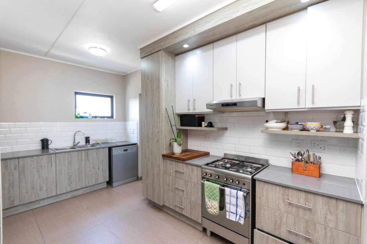 Modern kitchen featuring light wood-grain cabinetry, subway tile backsplash, stone countertops, and a stainless steel gas stove with an integrated extractor fan.