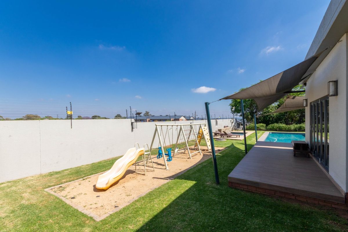 Spacious rear garden featuring a swimming pool, wooden decking with shade sails, and a secure perimeter wall with electric fencing.