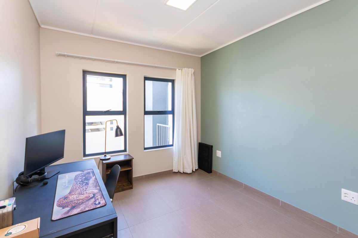 A well-maintained bedroom featuring neutral and accent-colored walls, tiled flooring, and large aluminium-framed windows providing natural light.