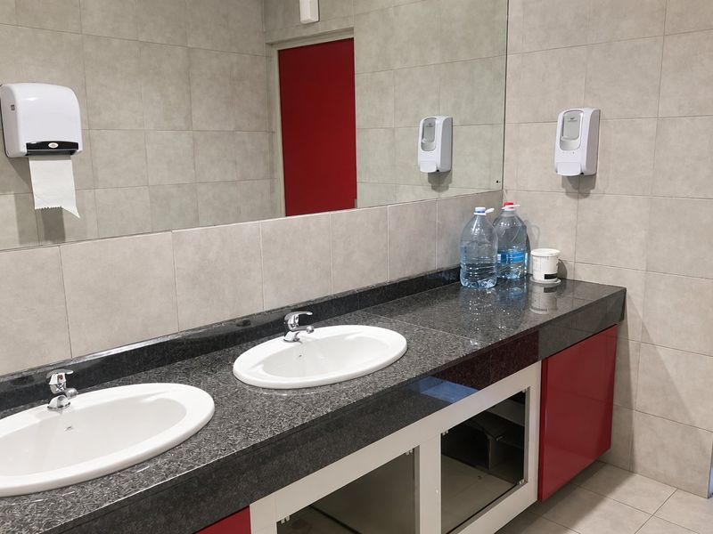 Commercial bathroom featuring a double vanity with granite countertop, tiled walls, and large mirror. Note the missing cabinet door under the vanity.
