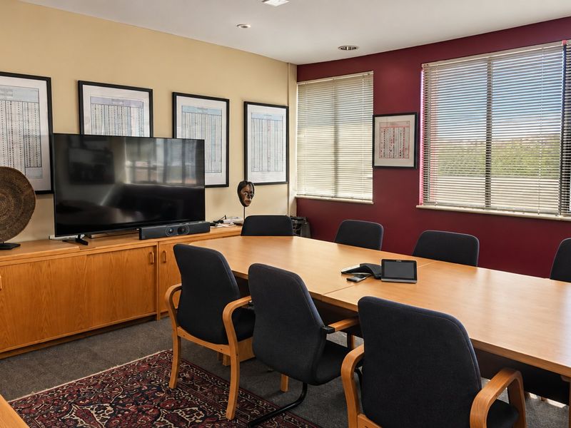 A professional commercial boardroom featuring built-in cabinetry, recessed lighting, and large windows with venetian blinds, providing a functional meeting space.