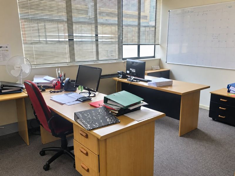 A functional commercial office space featuring carpeted flooring, large windows with venetian blinds, and a wall-mounted whiteboard.