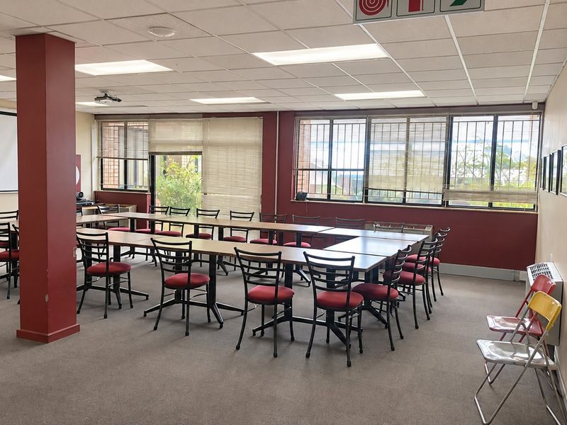 Spacious commercial office or meeting room featuring a suspended ceiling, large windows with security bars, and carpeted flooring, suitable for professional use.
