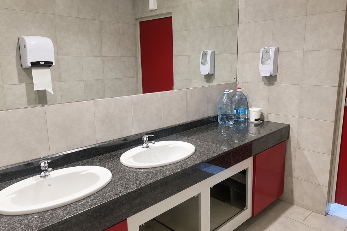 Commercial bathroom featuring a double vanity with granite countertop, tiled walls, and large mirror. Note the missing cabinet door under the vanity.