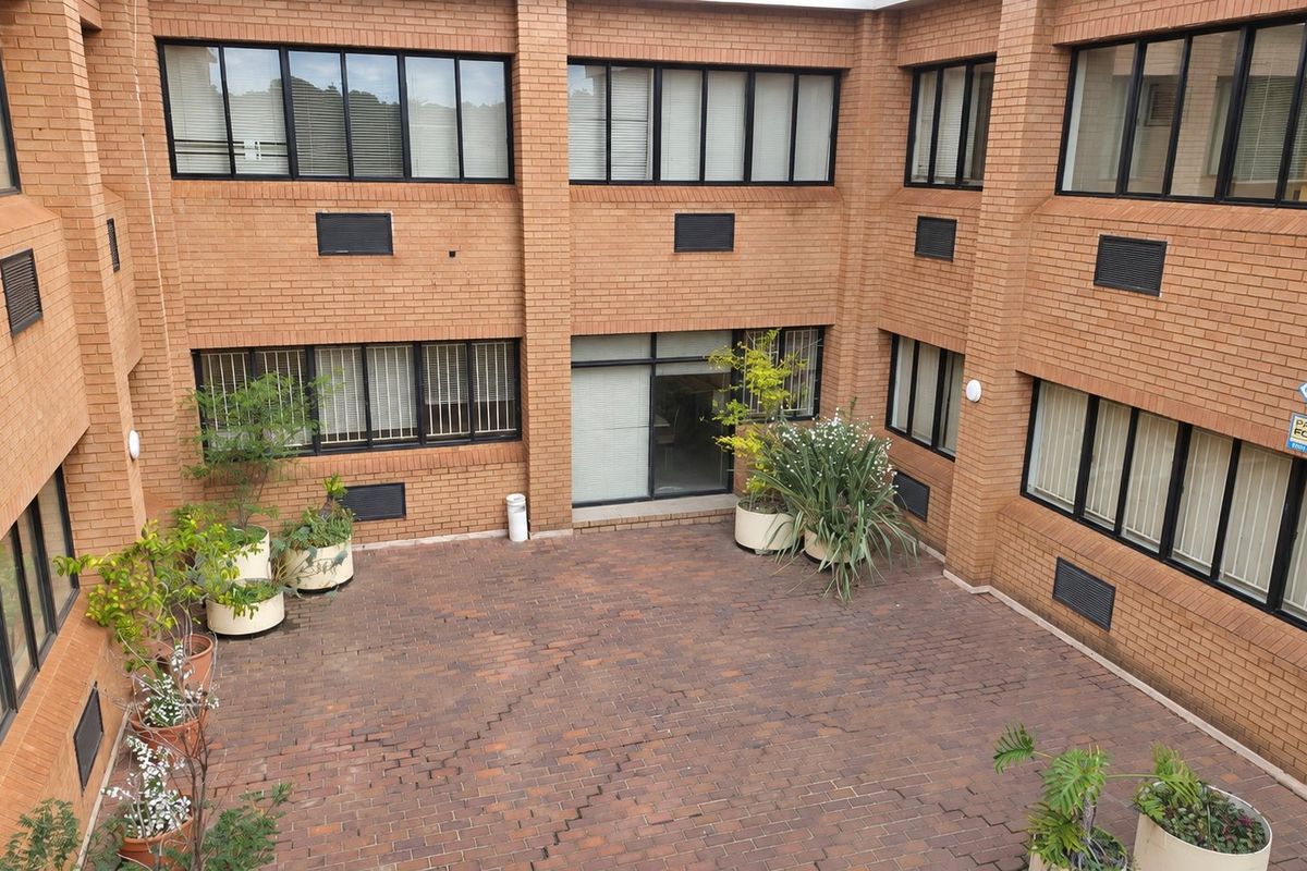 An enclosed brick courtyard featuring paved flooring and multiple office windows, providing a private outdoor space within the commercial building complex.