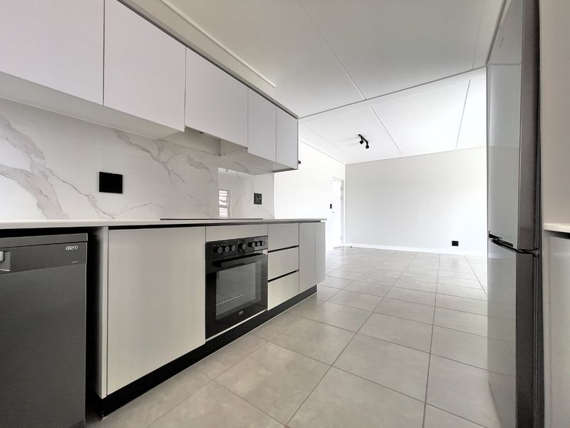Modern open-plan kitchen featuring sleek cabinetry, marble-look splashback, built-in oven, and neutral ceramic tile flooring in a bright, spacious living area.
