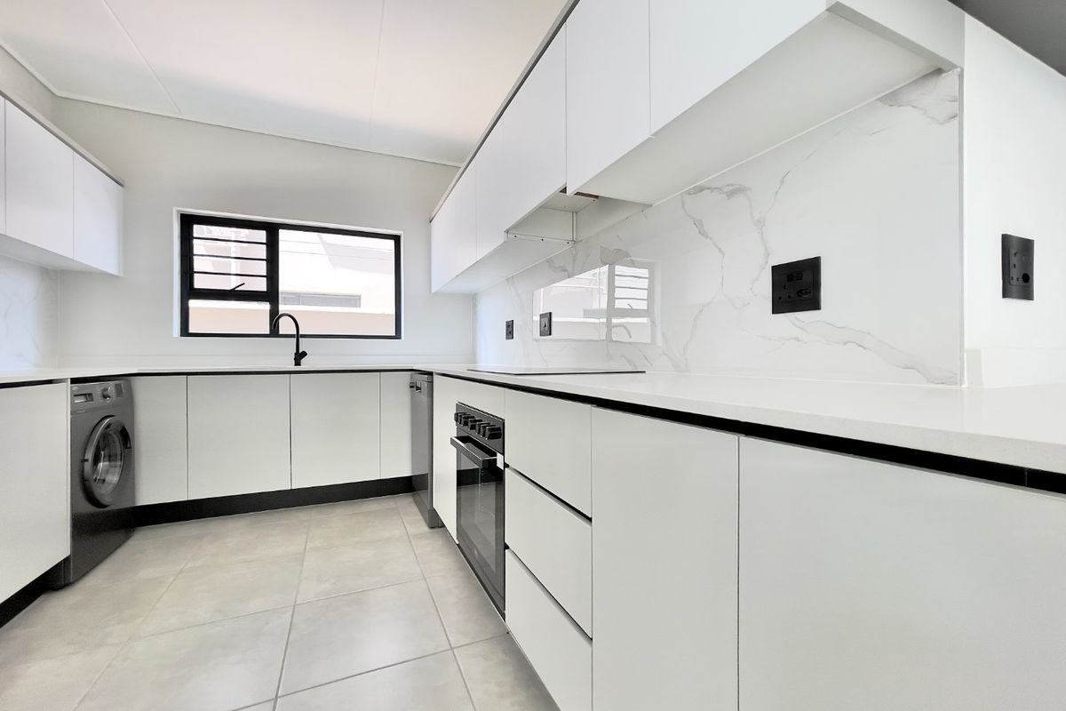 Modern kitchen featuring sleek white cabinetry, marble-look splashback, stone countertops, built-in oven, and integrated laundry plumbing in a clean, contemporary finish.