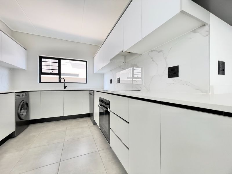 Modern kitchen featuring sleek white cabinetry, marble-look splashback, stone countertops, built-in oven, and integrated laundry plumbing in a clean, contemporary finish.