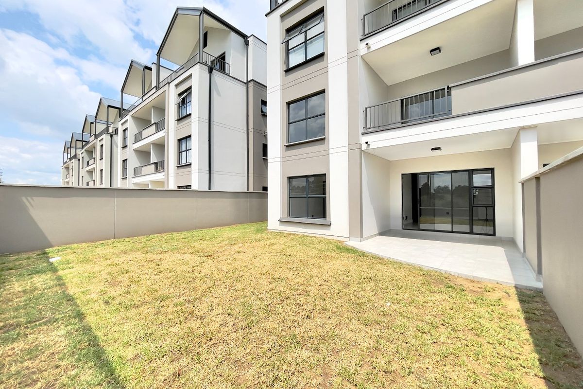 Rear view of a modern apartment complex featuring a private ground-floor patio, sliding glass doors, and a small enclosed garden area.