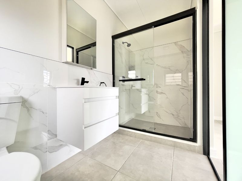 Modern bathroom featuring a wall-mounted vanity, walk-in shower with black frame, and elegant marble-look wall tiling.