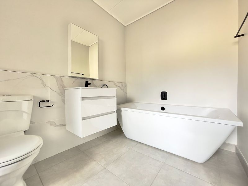 Modern bathroom featuring a sleek freestanding bathtub, wall-mounted vanity, and contemporary black tapware with elegant marble-look wall tiling.