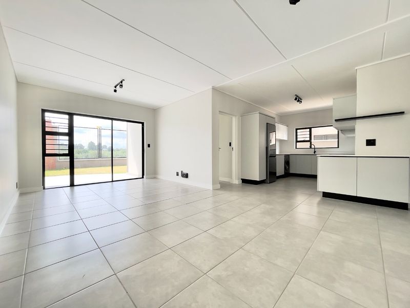 Modern open-plan living and kitchen area featuring neutral tiled flooring, sleek cabinetry, and large sliding doors leading to an outdoor space.