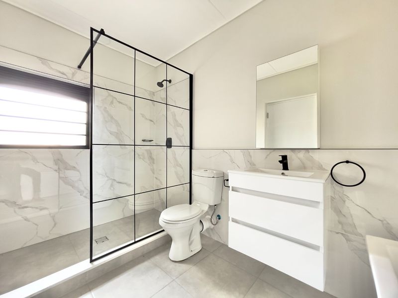 Modern bathroom featuring a walk-in shower with black-framed glass, a sleek wall-mounted vanity, and contemporary marble-look wall tiling.