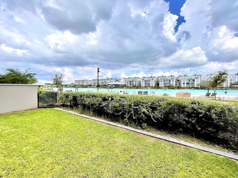 A view of a communal swimming pool area featuring a well-maintained lawn and landscaped garden borders within a residential apartment complex.