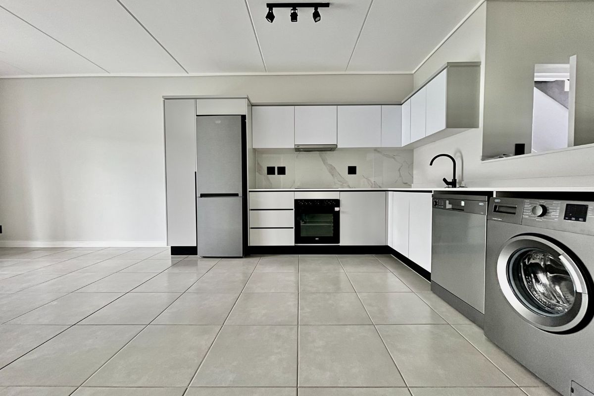 Modern, clean-lined kitchen featuring white cabinetry, marble-look backsplash, integrated oven, and sleek ceramic floor tiles in an open-plan layout.