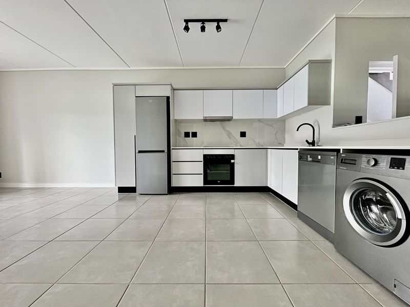 Modern, clean-lined kitchen featuring white cabinetry, marble-look backsplash, integrated oven, and sleek ceramic floor tiles in an open-plan layout.
