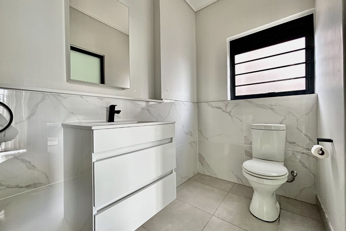 Modern bathroom featuring a sleek white vanity with black tapware, marble-look wall tiles, and a clean, minimalist design.