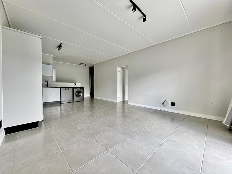 Spacious open-plan living area featuring tiled flooring, track lighting, and a functional kitchen with built-in cabinetry and appliance connections.