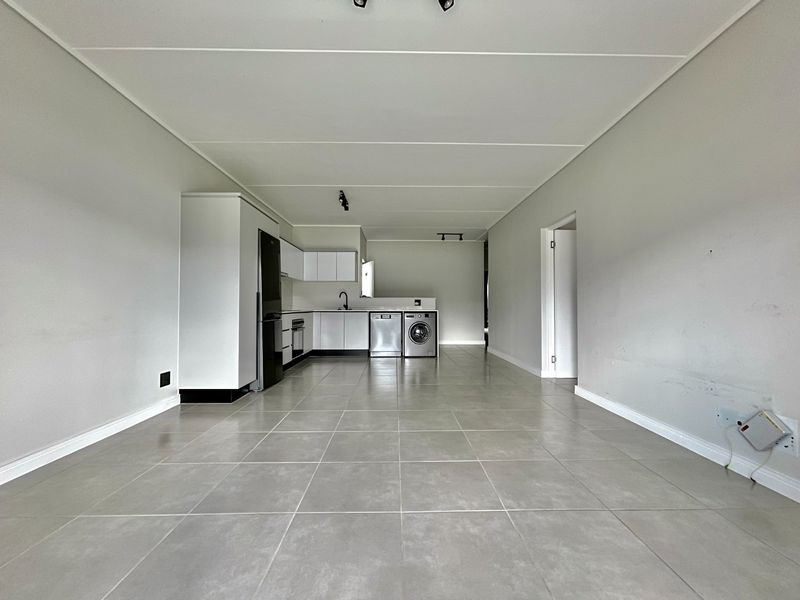 Spacious open-plan kitchen and living area featuring neutral tiled flooring, modern cabinetry, and integrated appliances in a clean, vacant setting.