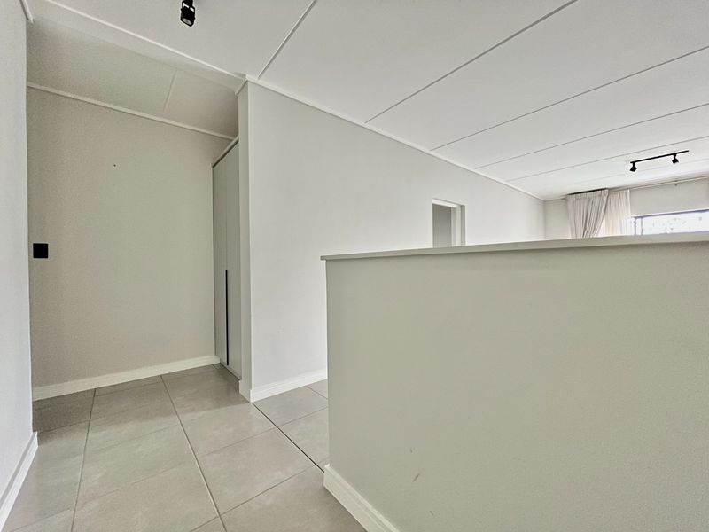 A bright, neutral hallway featuring tiled flooring, built-in storage cabinetry, and modern track lighting, providing a clean and functional transition space.