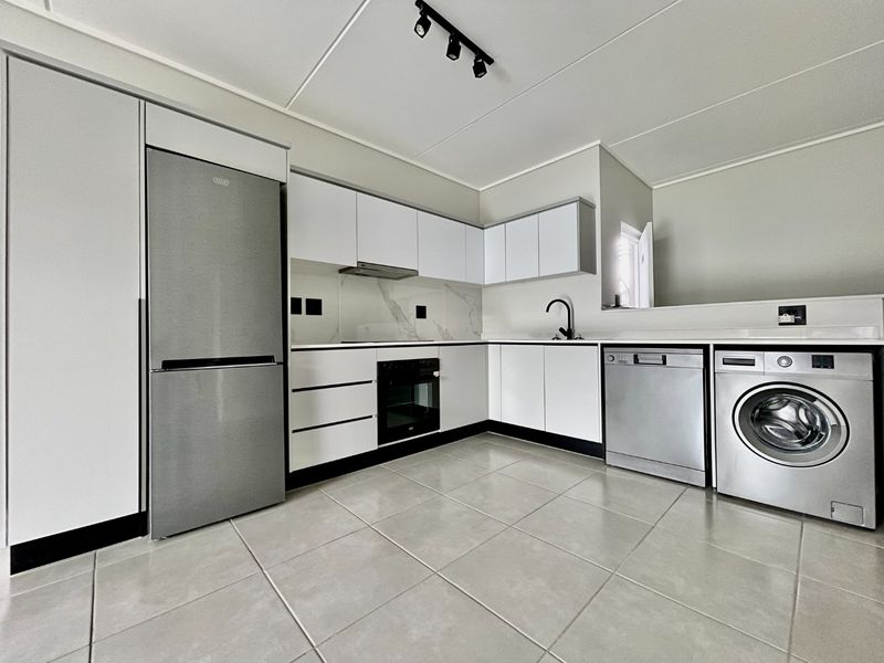 Modern kitchen featuring sleek white cabinetry, stone countertops, integrated oven, extractor fan, and tiled flooring with contemporary black fixtures.
