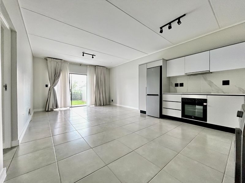 Modern open-plan living area featuring tiled floors, sleek kitchen cabinetry with built-in appliances, and direct access to an outdoor space through sliding glass doors.